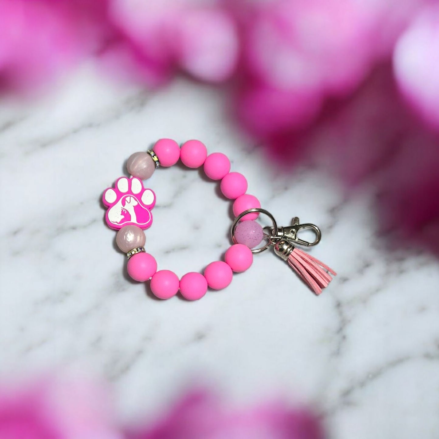 Pink beaded keychain with a cat/dog paw print focal bead on a marble surface with pink flowers in the background.