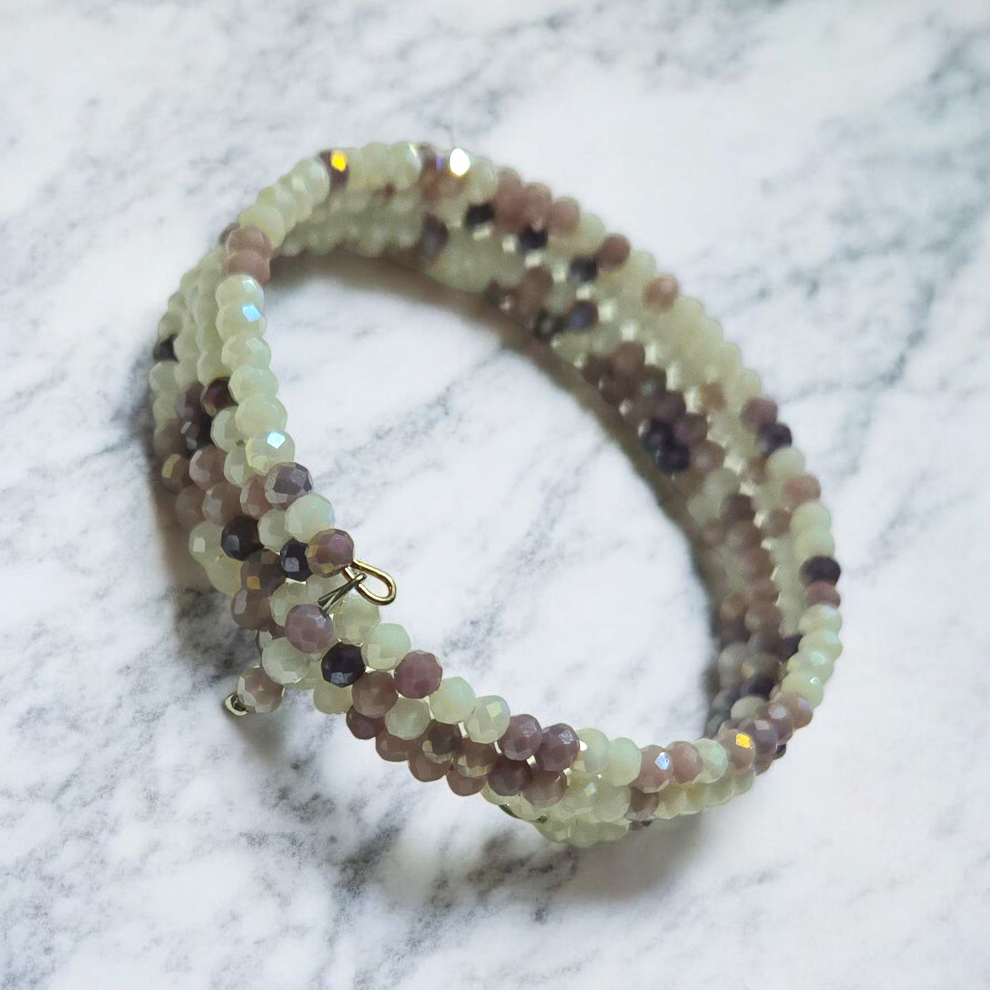 Purple and White crystal memory wire bracelet displayed on light marble surface.