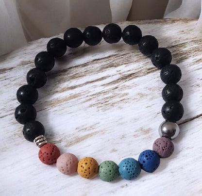 Chakra inspired lava stone bracelet with multicolor beads, black lava stones, stainless steel accent bead, and zinc alloy spacer on a white background.