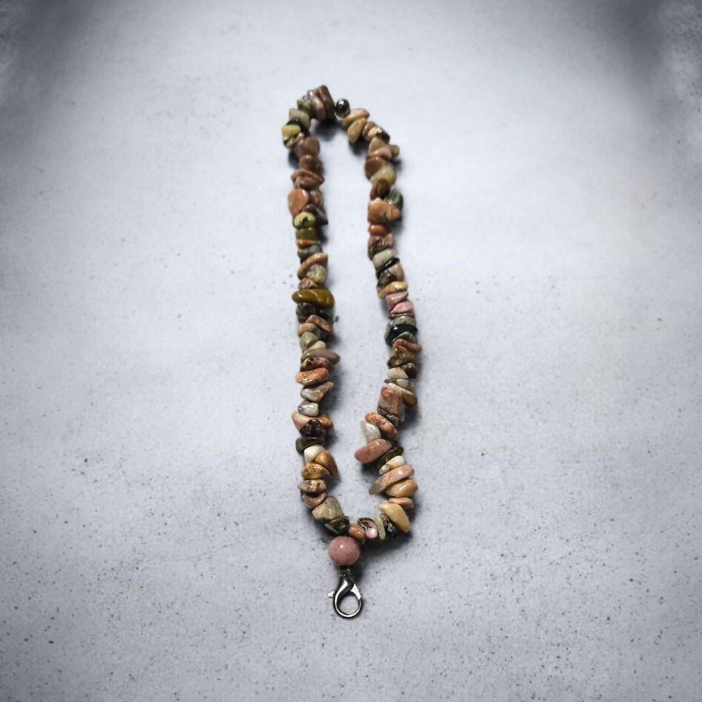 A phone lanyard made of Rhodonite stone chip beads displayed on a light marble surface.  Photo and lanyard made by Divalicious Designs.