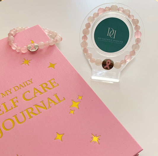 A rose quartz bracelet with a breast cancer awareness charm on a pink journal .