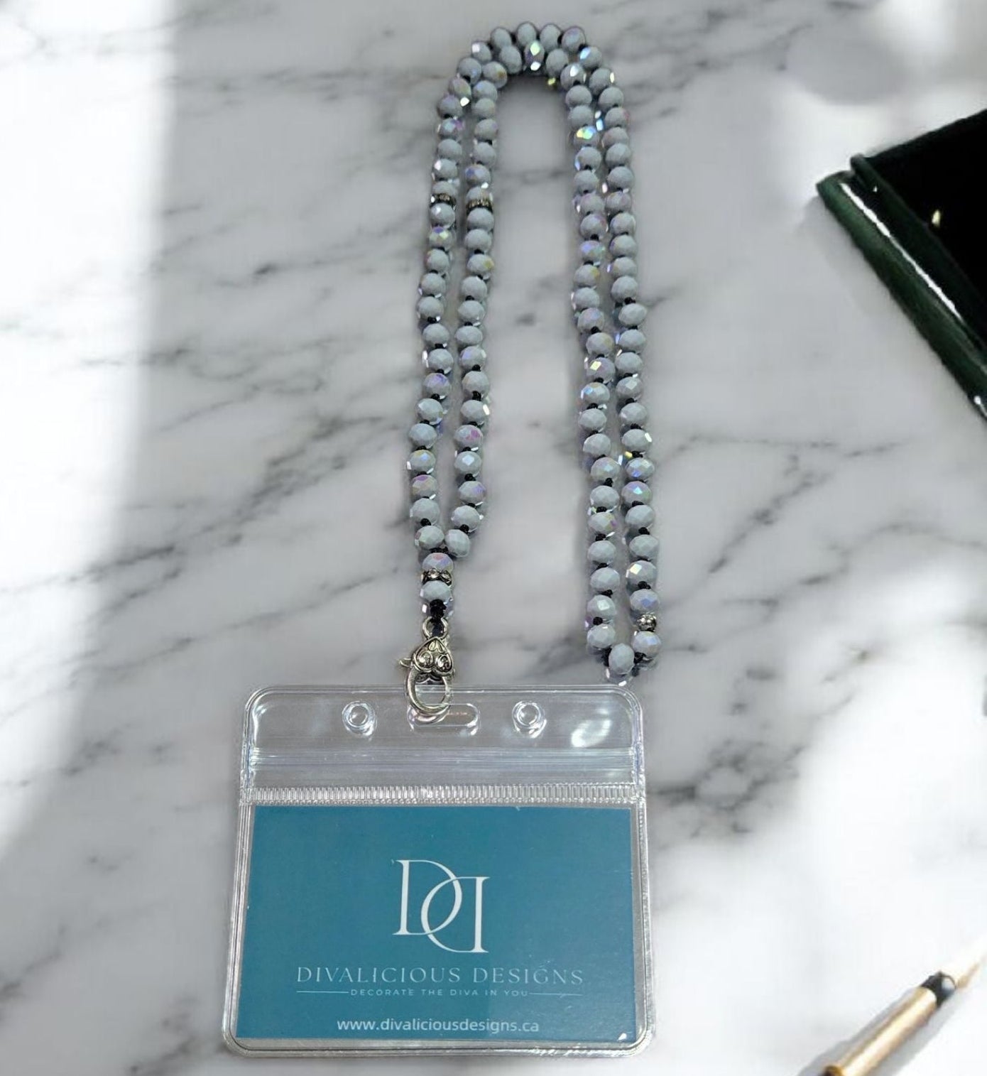 Gray beaded crystal lanyard with a clear badge holder on a marble surface