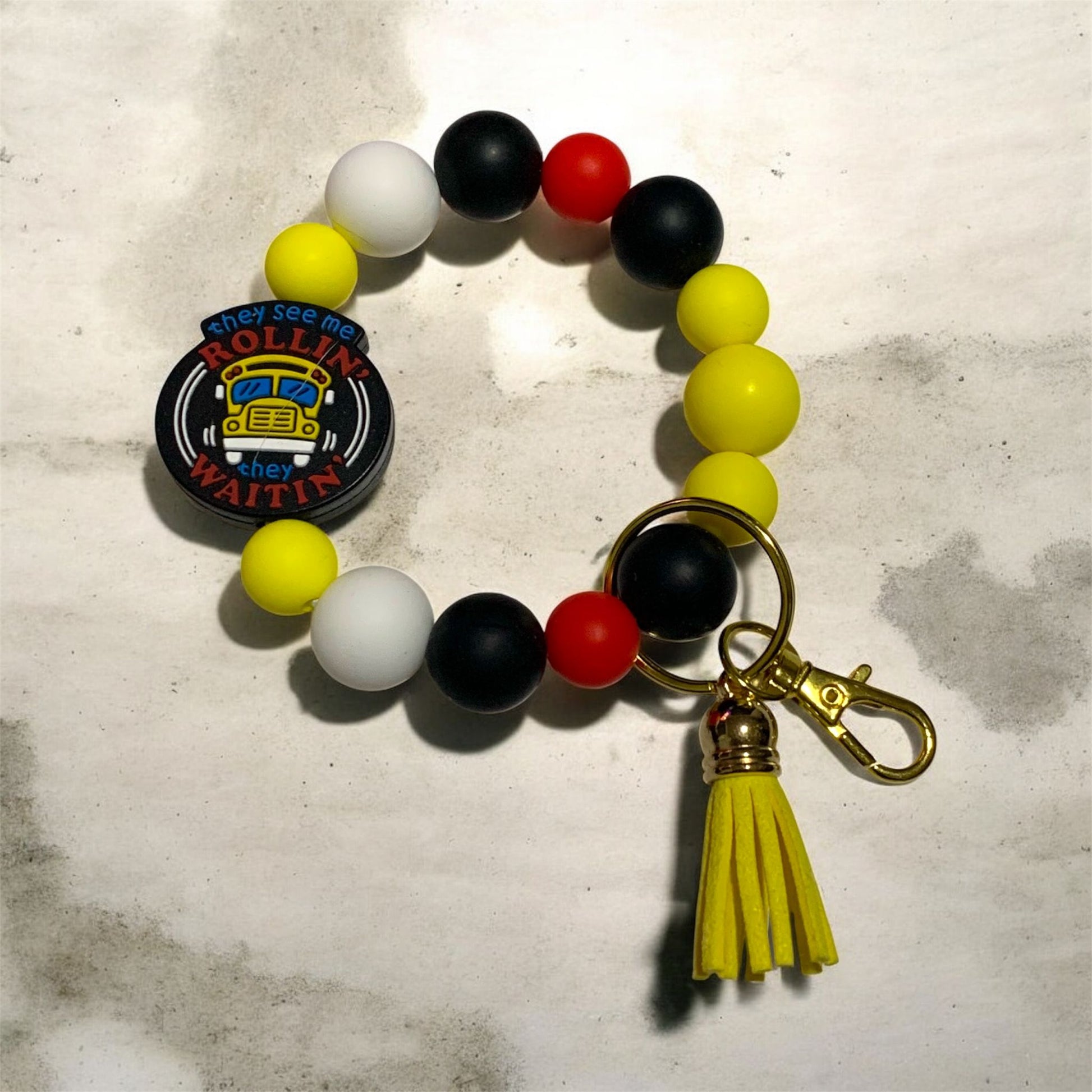Colorful silicone beaded keychain bracelet with a tassel on a textured surface. The theme of the keychain is for a school bus, perfect for a bus driver. 