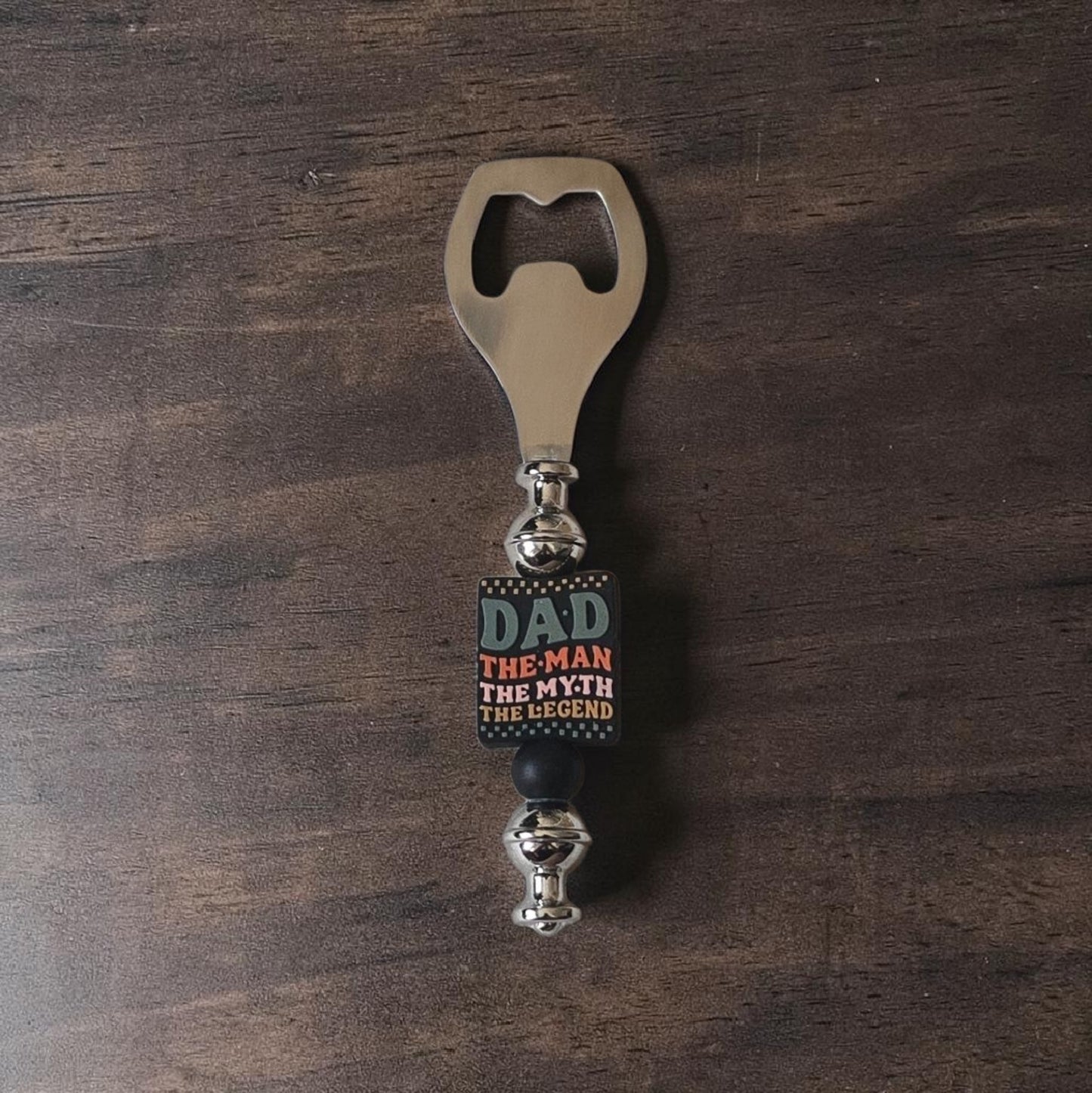 Handmade steel and Silicone Bottle opener with 'Dad, The Man, The Myth, The Legend' text on a wooden surface. Made by Divalicious Designs in Mississauga 