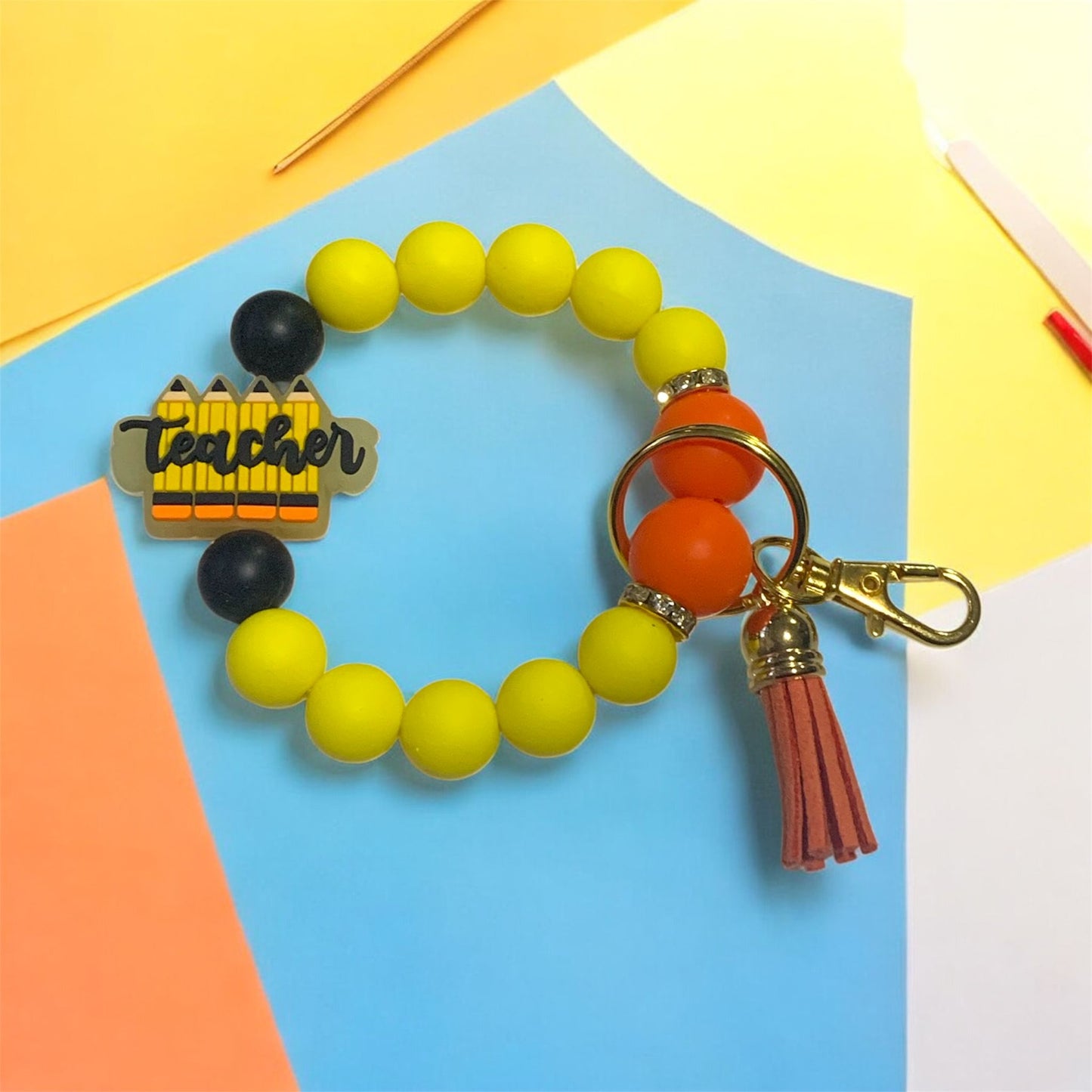 Yellow Orange and black silicone beaded keychain wristlet with 'Teacher' charm on a colorful background