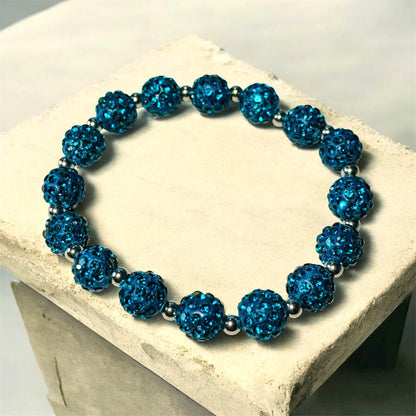 A Bracelet made of Teal Shamballa beads and stainless steel beads laying on a light stone surface. Picture and bracelet by Divalicious Designs.