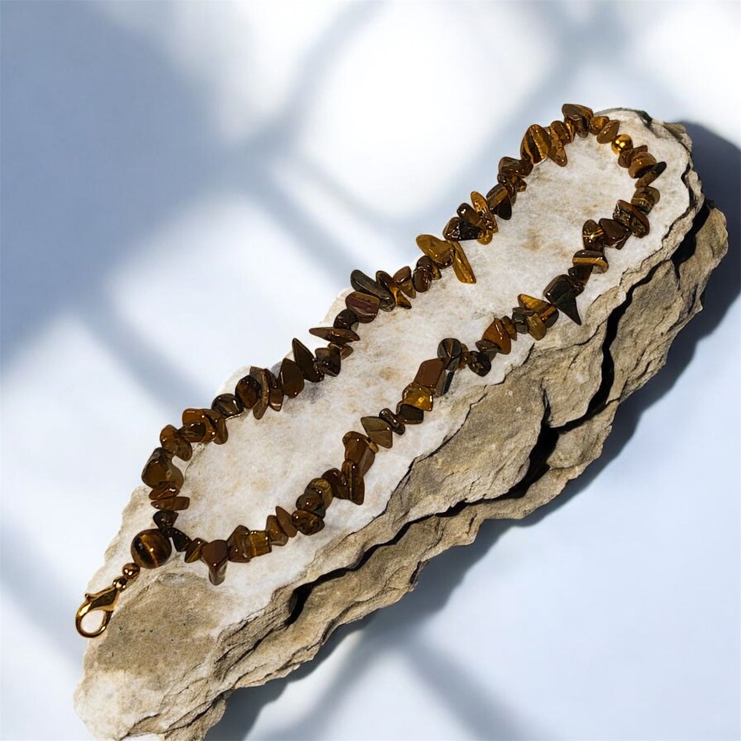 A phone lanyard made from Tiger's Eye Stone Chip Beads, displayed on a long stone surface. Photo and lanyard made by Divalicious Designs.