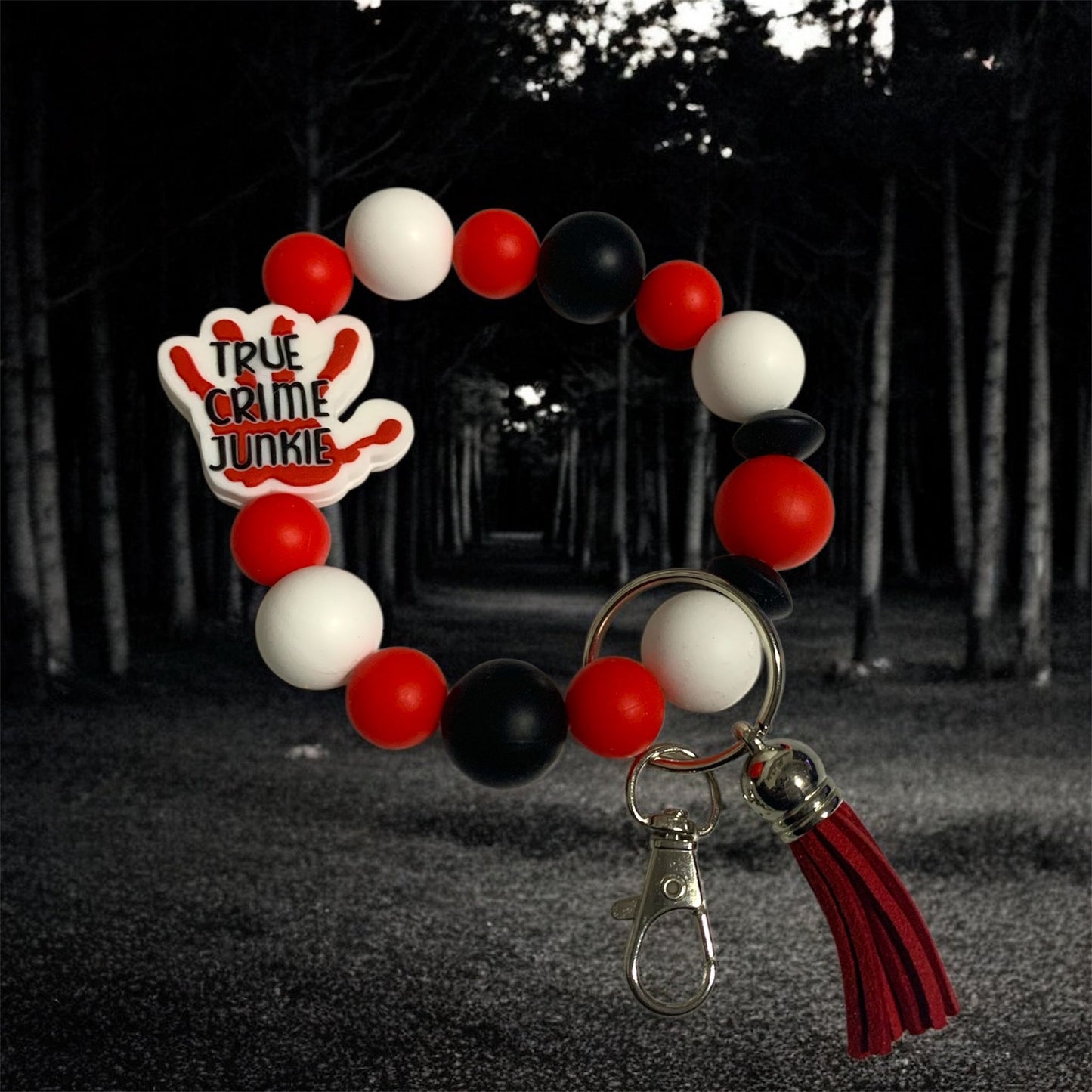 Keychain with red, white, and black balloons and 'True Crime Junkie' logo against a dark forest background.