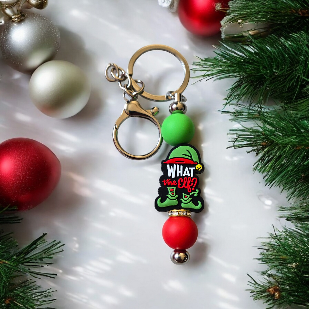Keychain with elf design surrounded by Christmas ornaments and greenery