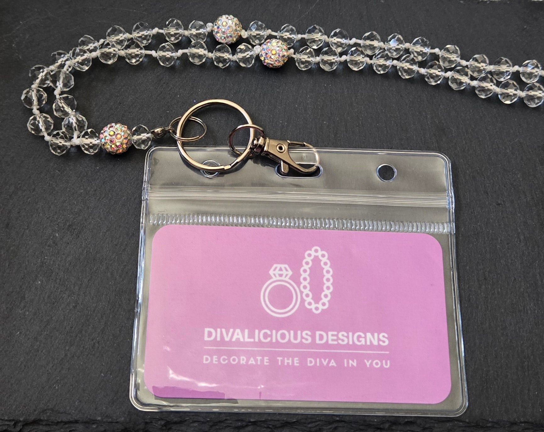 Clear beaded lanyard with a pink ID badge holder on a dark background.