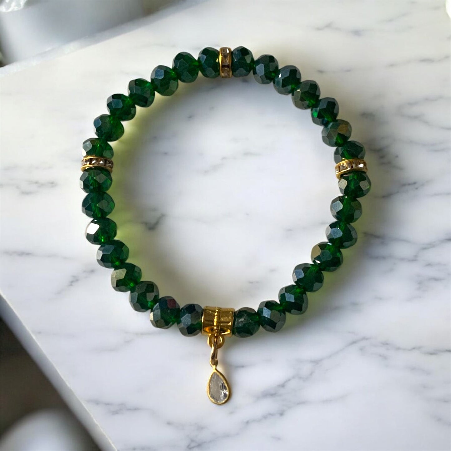 Green Austrian crystal bracelet with emerald coloured beads, gold accents, and a cubic zirconia teardrop charm displayed on a light marble surface.