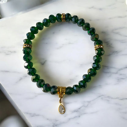 Green Austrian crystal bracelet with emerald coloured beads, gold accents, and a cubic zirconia teardrop charm displayed on a light marble surface.