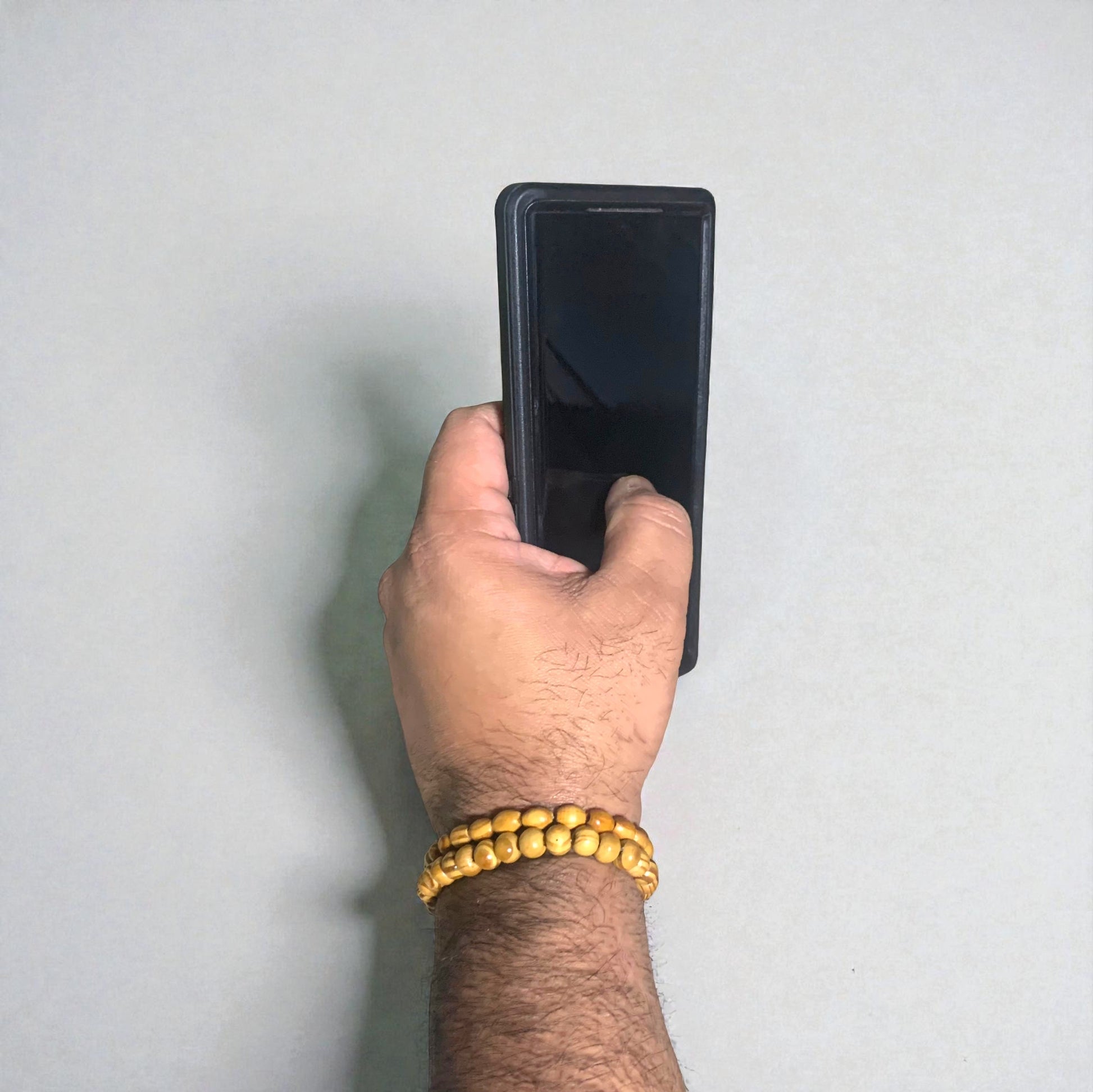 Hand holding a black smartphone against a light gray background. The focal point is a set of two men's wooden bracelets.